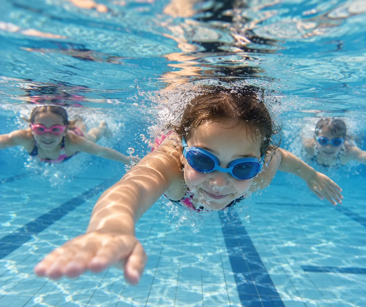 Lachende Kinder mit Schwimmbrillen tauchen durchs Wasser